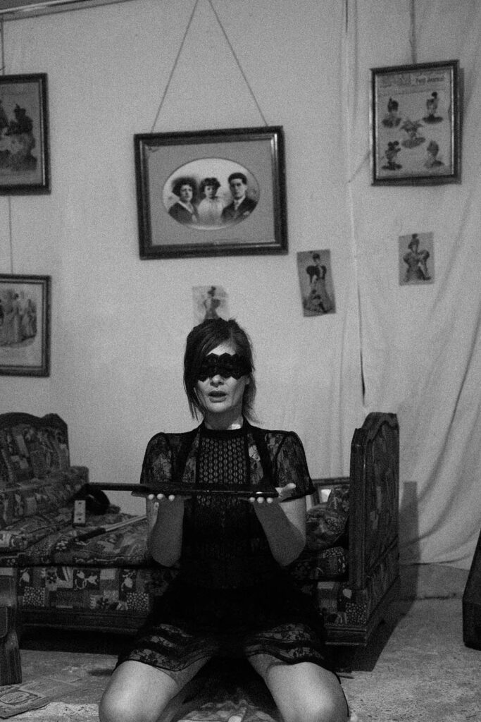 Une femme a genoux les yeux bandés, tenant un paddle entre ces mains, en offrande a son dominateur. Esthétique du désir, l'Amour et la violence x Fessée artisanale