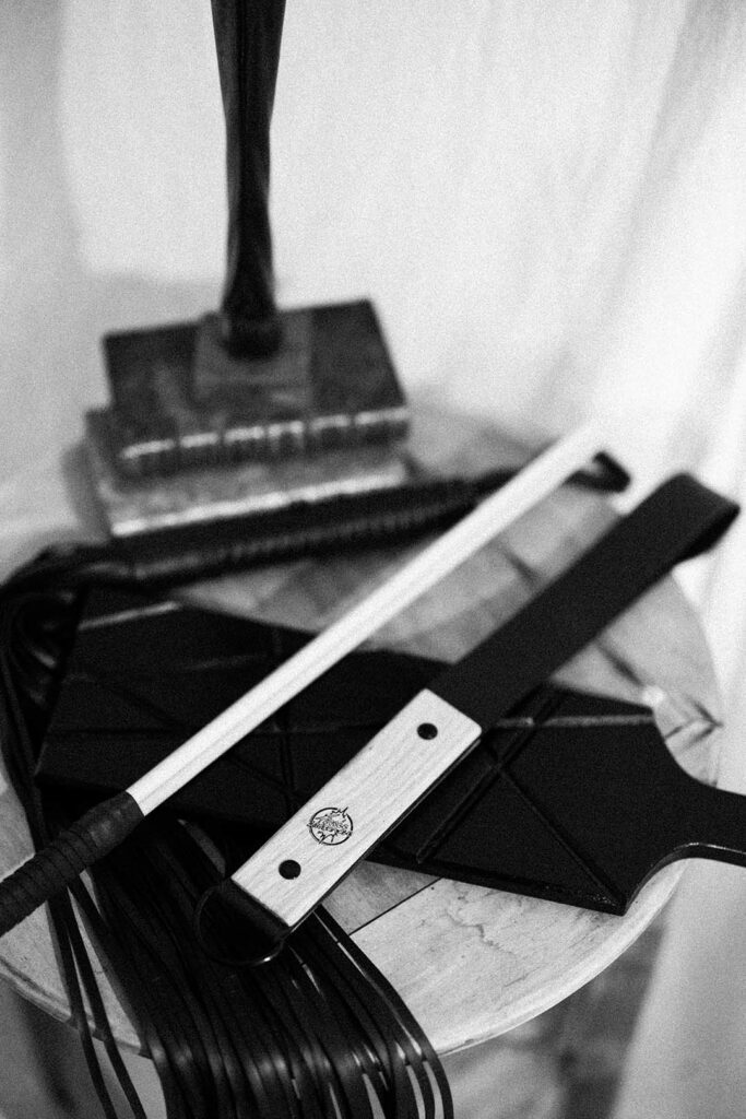 photo des objets fessée artisanale, la Frapett, une badine, un paddle et martinet posé sur une table de chevet. Esthétique du désir, l'Amour et la violence x Fessée artisanale