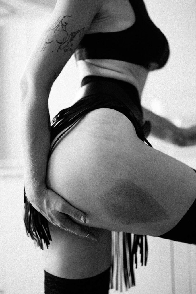 photo montrant le corps d'une femme qui porte la jupe frangine de la fessée artisanale. Ca main retire les franges de la jupe pour montrer une marque sur sa fesse. Esthétique du désir, l'Amour et la violence x Fessée artisanale