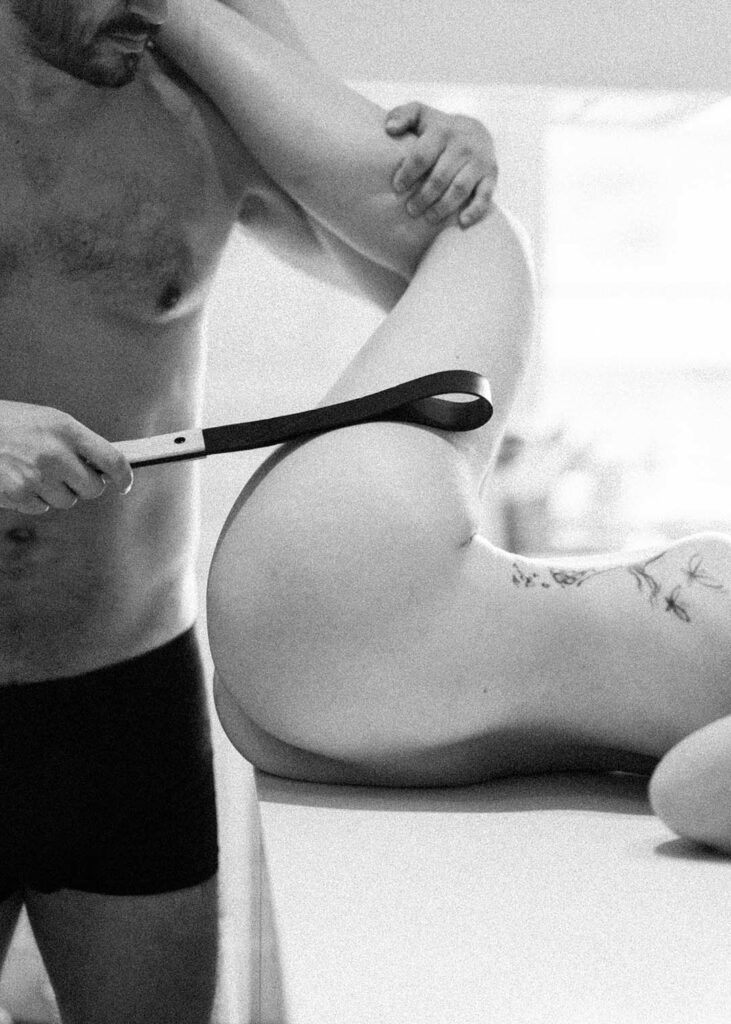 gros plan d'une Frapett, le ceinturon de la fessée artisanale, porté" par une main d'homme qui s'abat sur les fesses de sa compagne, image de complicité. Esthétique du désir, l'Amour et la violence x Fessée artisanale