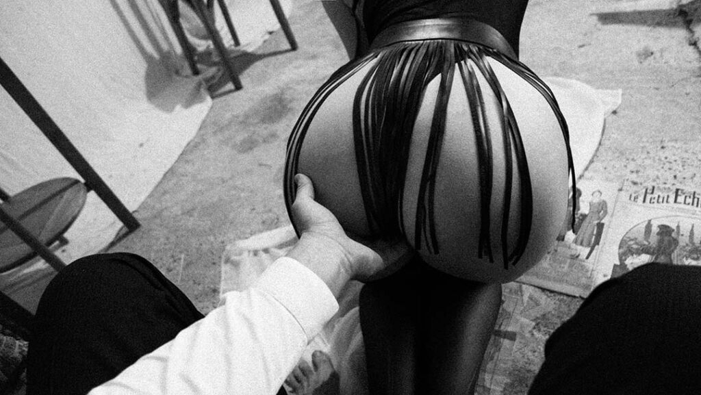 gros plan d'une main d'homme caressant l'entre jambe de sa compagne. Vue plongeante sur les fesses de celle ci qui porte la jupe a frange de la fessée artisanale. Esthétique du désir, l'Amour et la violence x Fessée artisanale