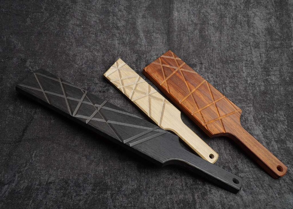 Photo sur fond noir montrant la gamme des Paddles choc de Fessée Artisanale en chêne