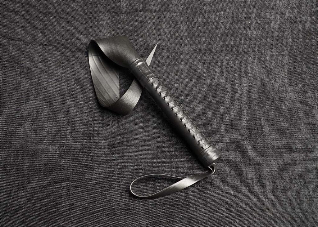 photo montrant un "draakanga", paddle bdsm artisanale en caoutchouc "LA langue de dragon" de la marque Fessée Artisanale avec un tressages "corset" sur fond sombre