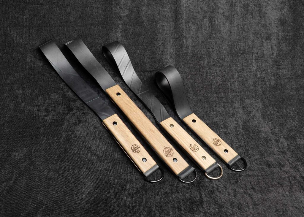 photo montrant la gamme de Paddles "Frapett" manche chêne et bande caoutchouc de la marque Fessée Artisanale sur fond sombre