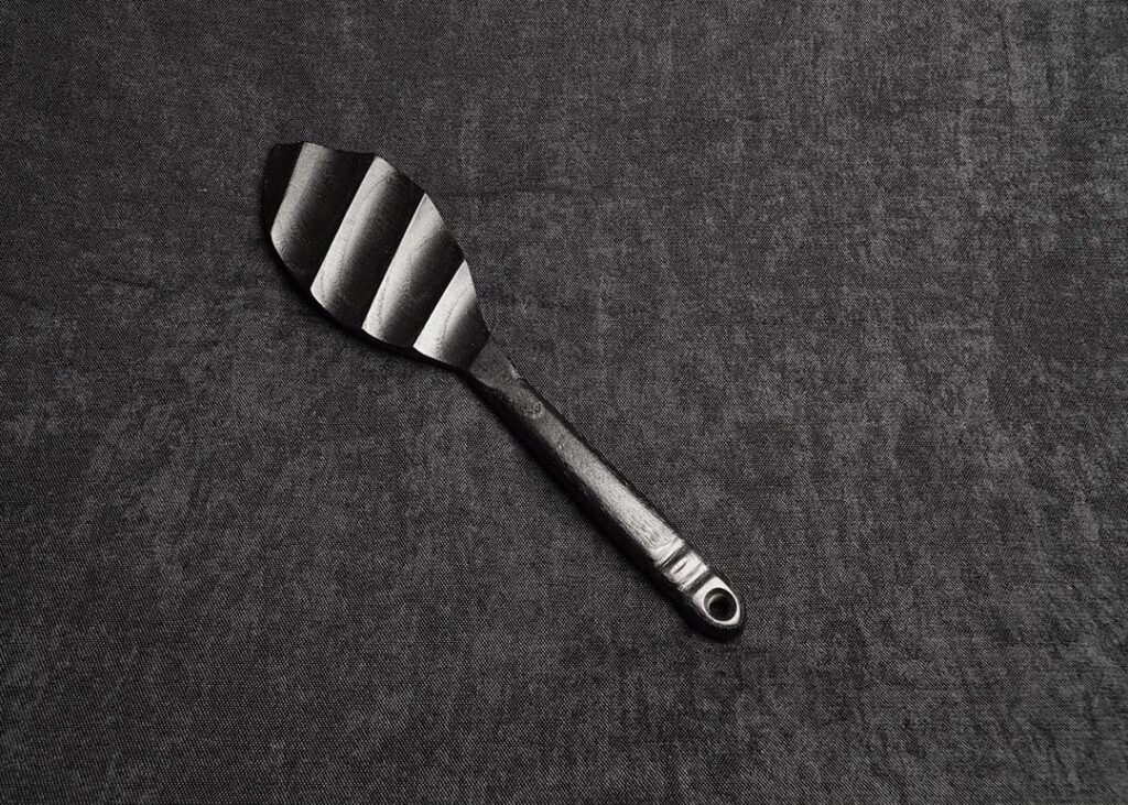 photo montrant le Paddle Lorier en chêne teinté noir de la marque Fessée Artisanale sur fond sombre