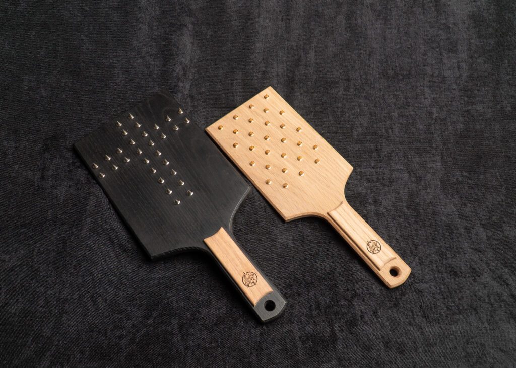 Photo montrant deux Paddles Vampire avec pics de la marque fessée artisanale sur fond sombre