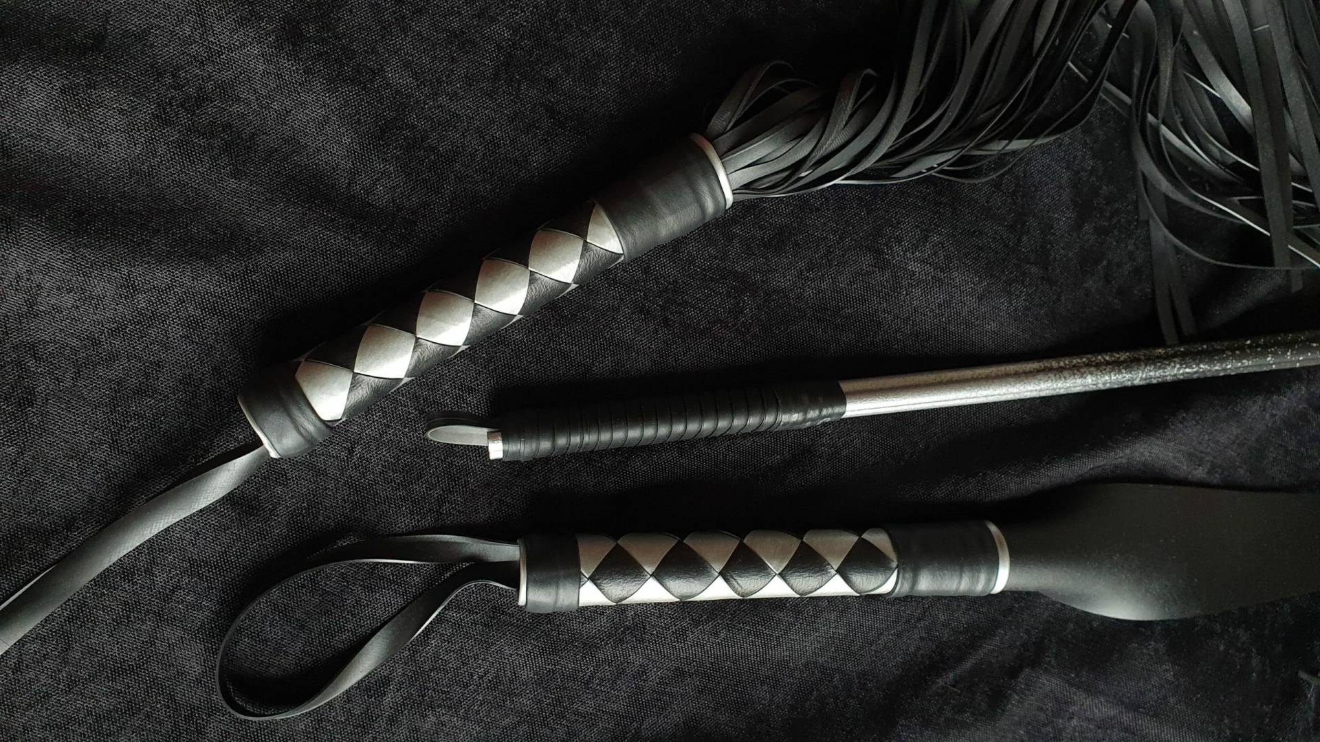 set d'outil (langue de dragon, martinet et badine) noir et argenté posé sur un fond noir velour
